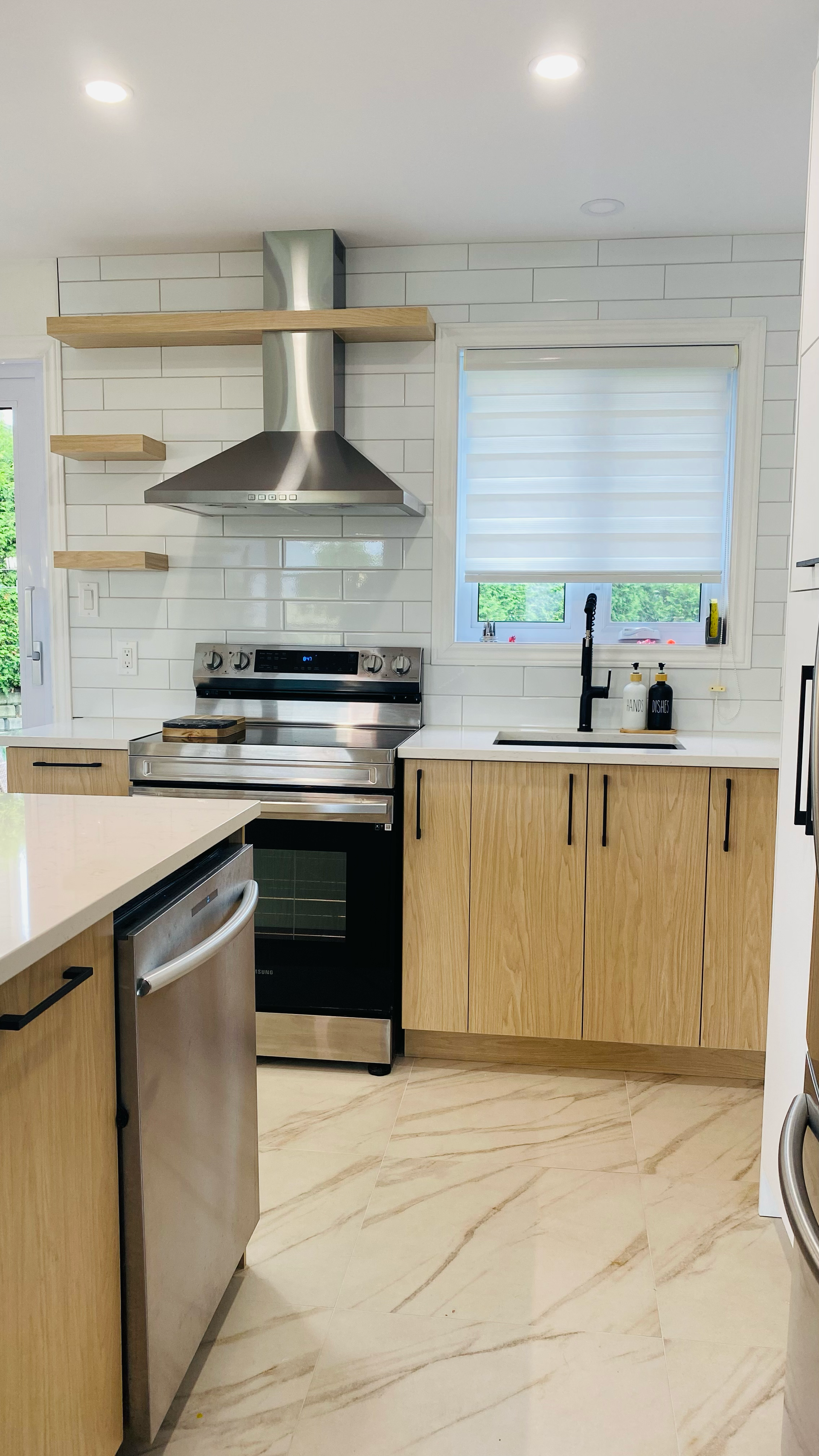 Cuisine moderne avec appareils électroménagers en acier inoxydable, armoires en bois clair et crédence en briques blanches.