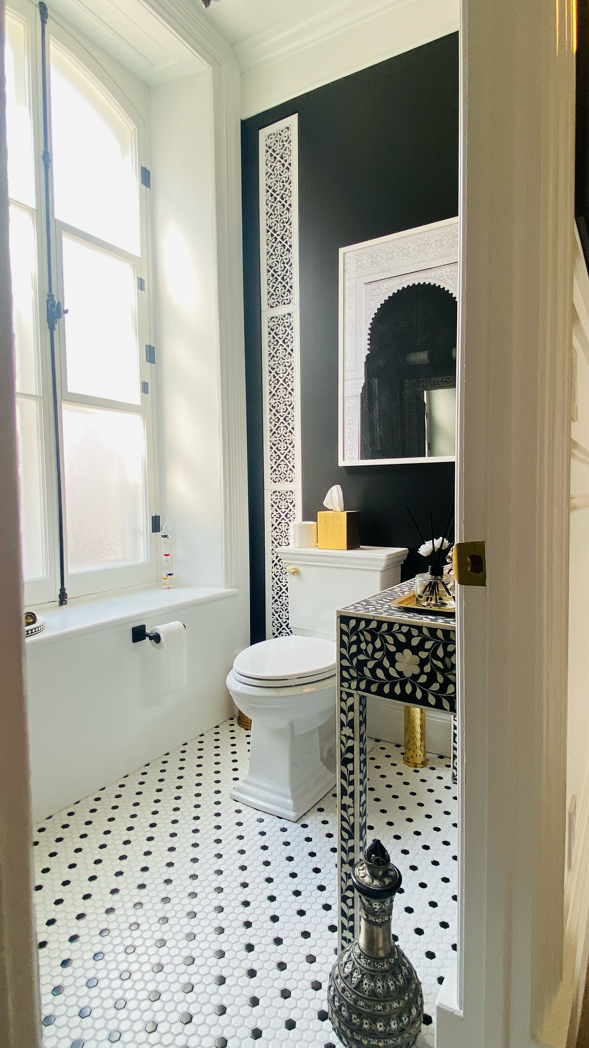Salle de bains avec sol carrelé en noir et blanc, toilettes, meuble-lavabo et mur d'accent noir.