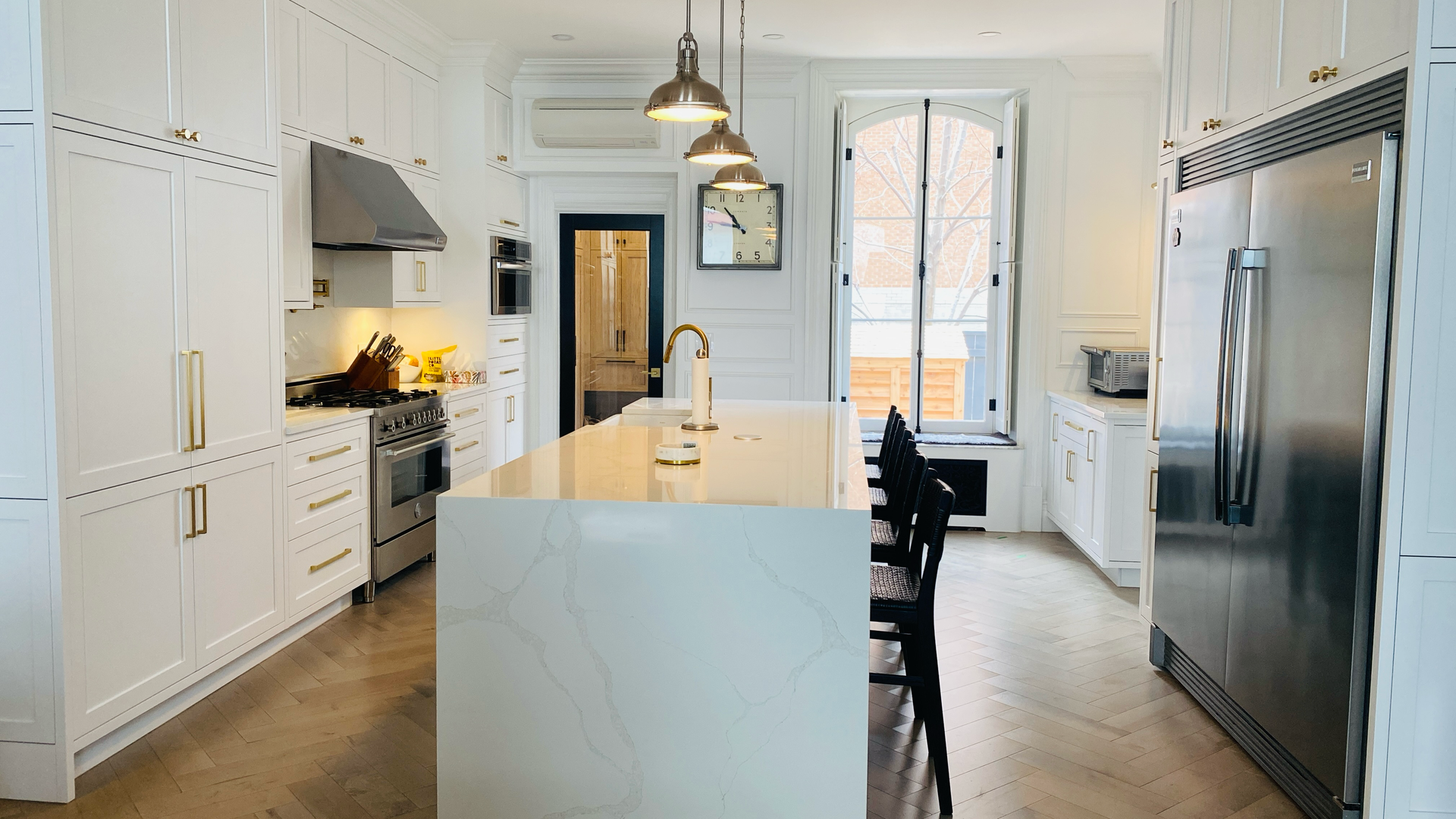 Cuisine blanche avec îlot central, électroménagers en acier inoxydable et quincaillerie dorée.