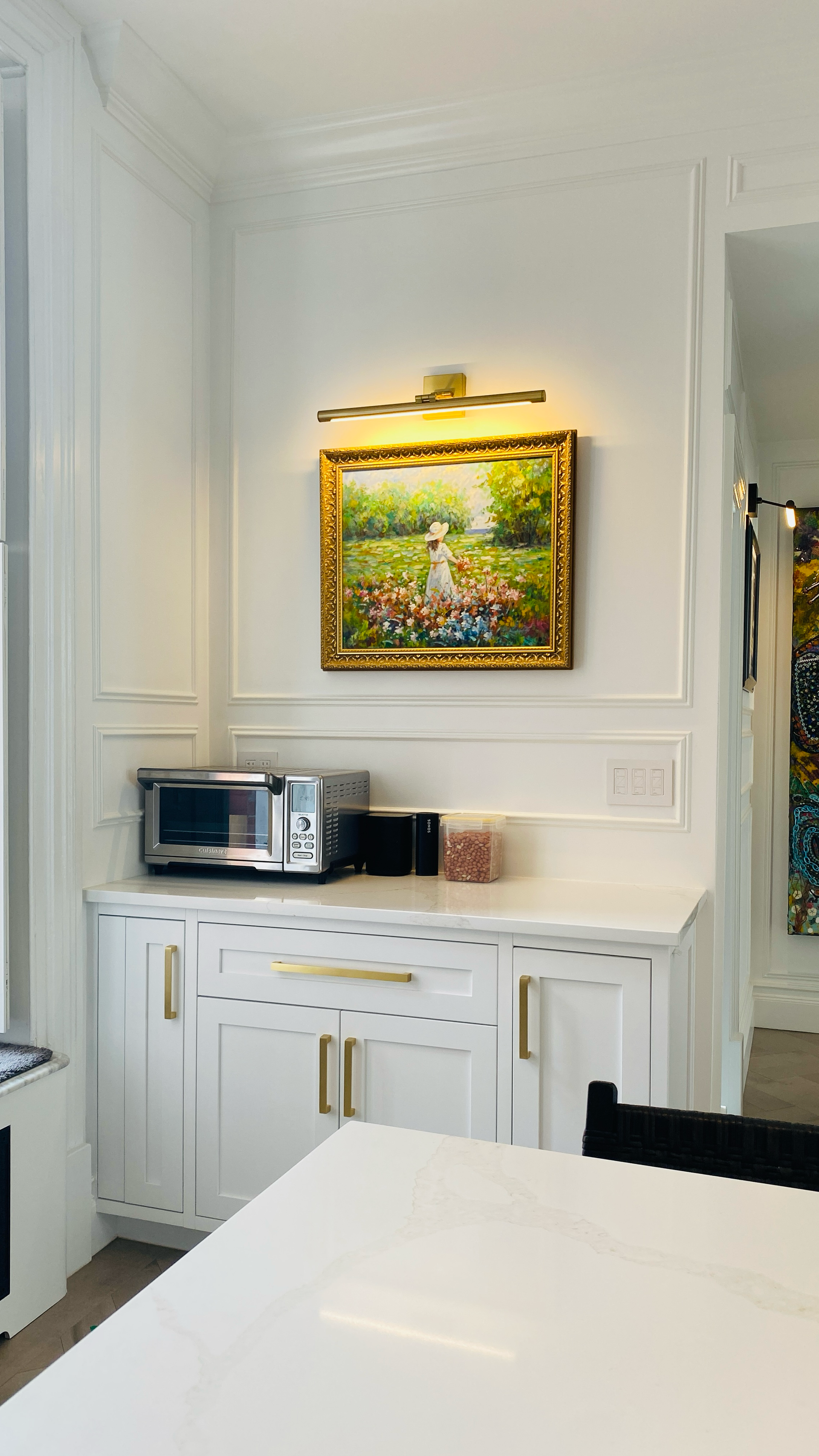 Meuble encastré blanc avec micro-ondes, grille-pain, tableau représentant un champ et accents dorés.