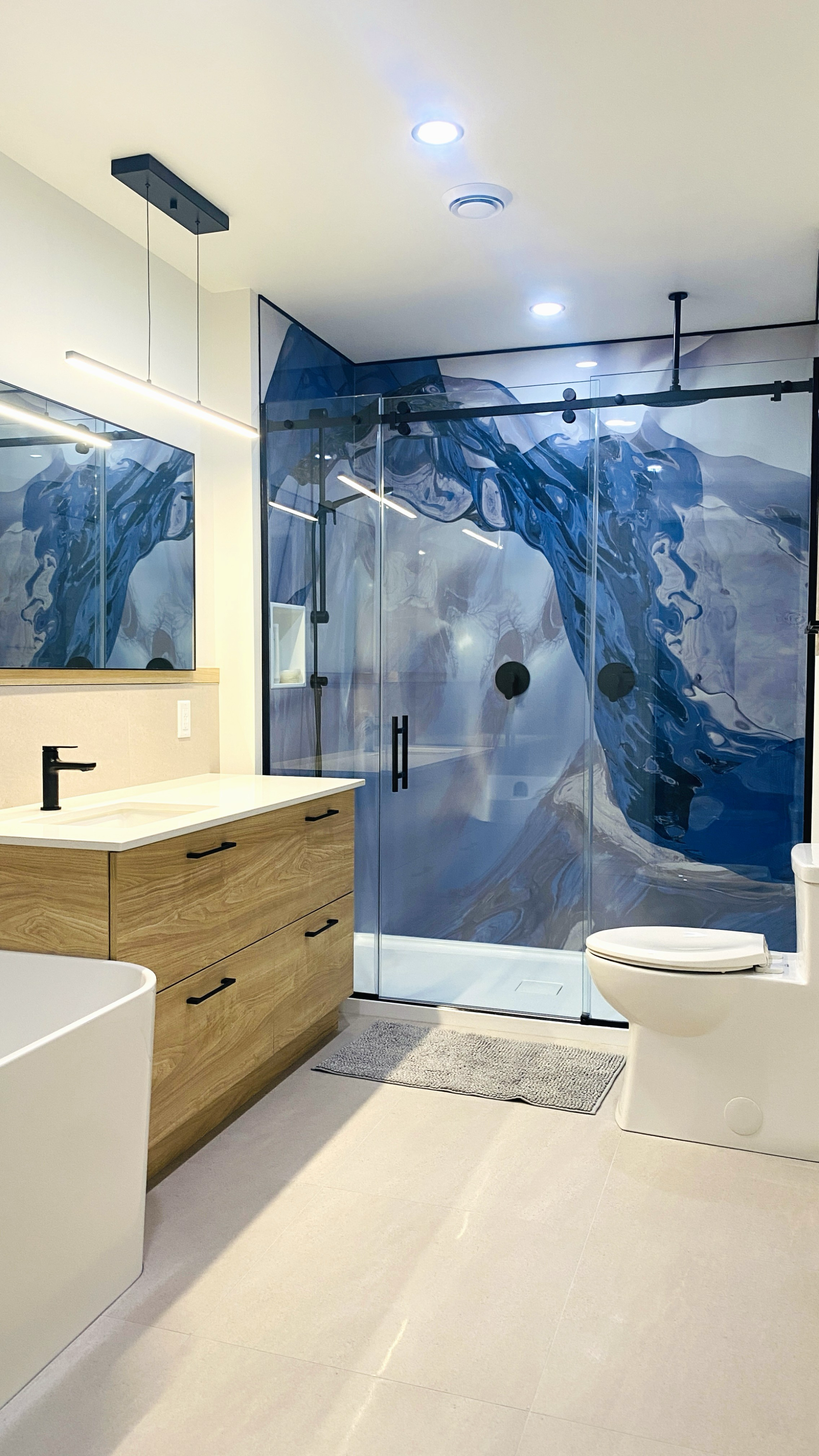 Salle de bains moderne avec douche à motifs bleus et blancs, meuble-lavabo en bois et toilettes blanches.
