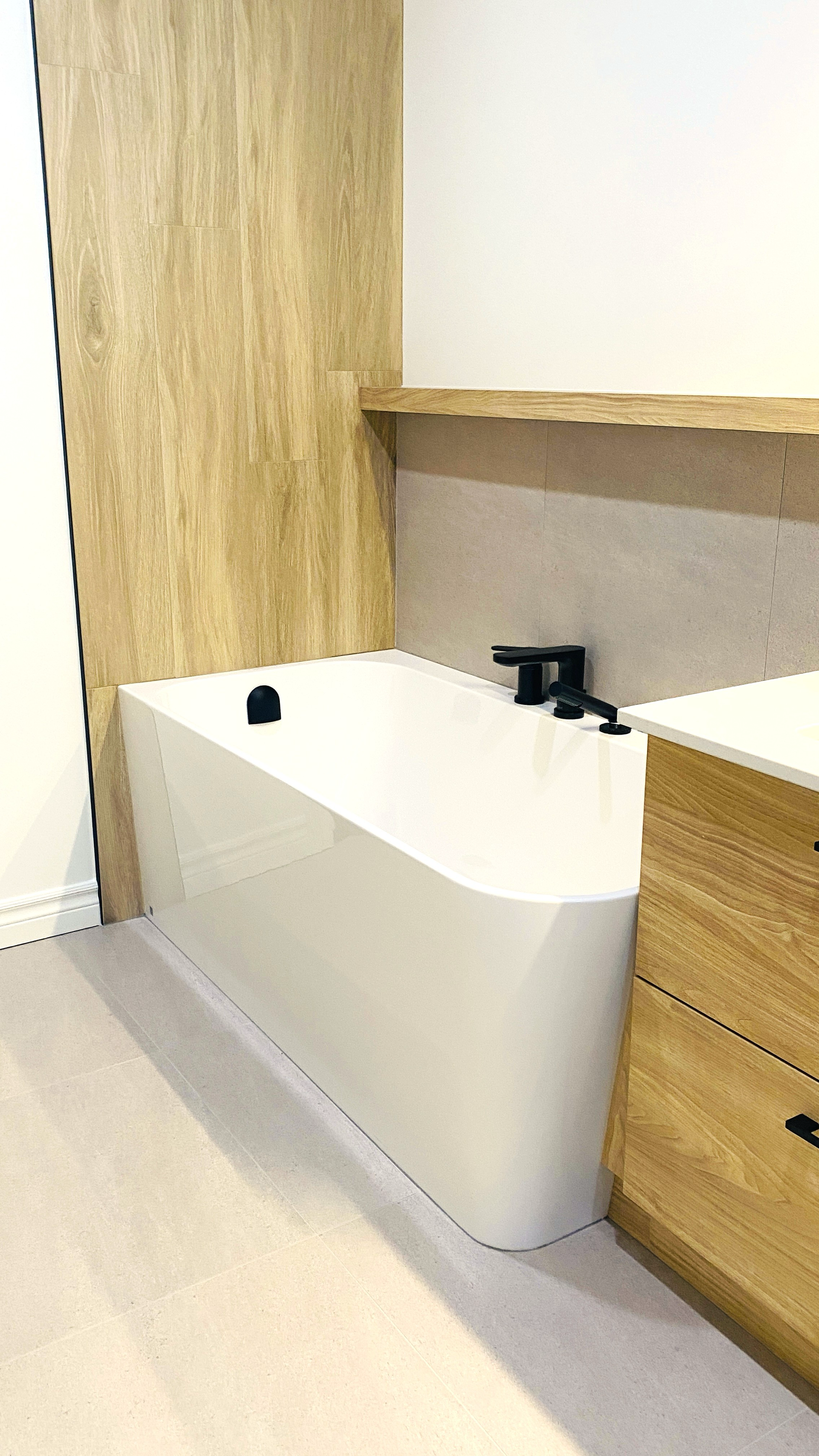 Baignoire blanche moderne dans une salle de bains avec des éléments en bois et des accessoires noirs.