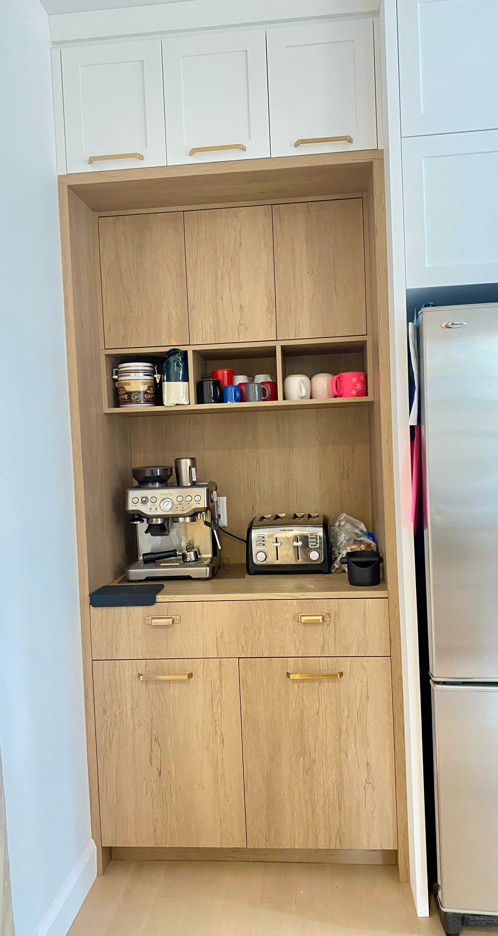 Meuble de cuisine intégré avec cafetière, grille-pain et étagères de rangement dans une cuisine moderne.