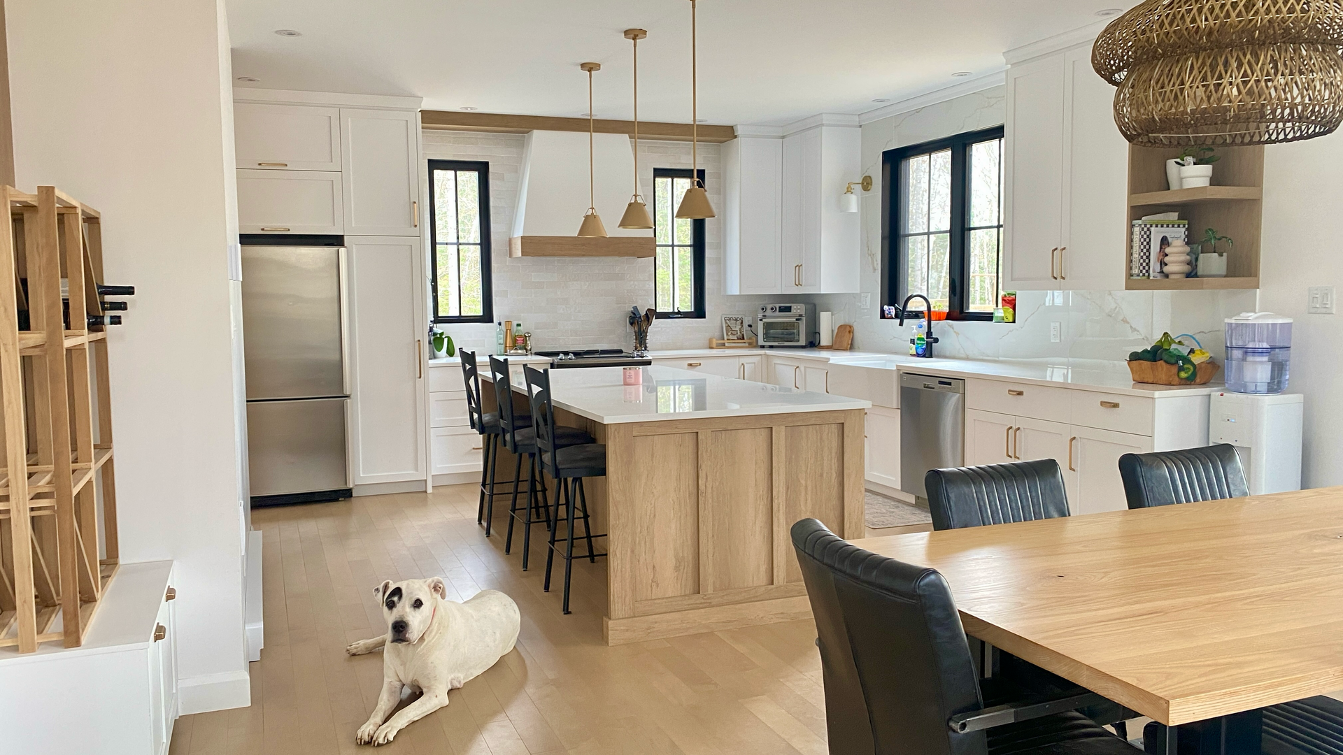 Cuisine blanche spacieuse avec des touches de bois clair, un réfrigérateur en acier inoxydable et un chien allongé sur le sol.
