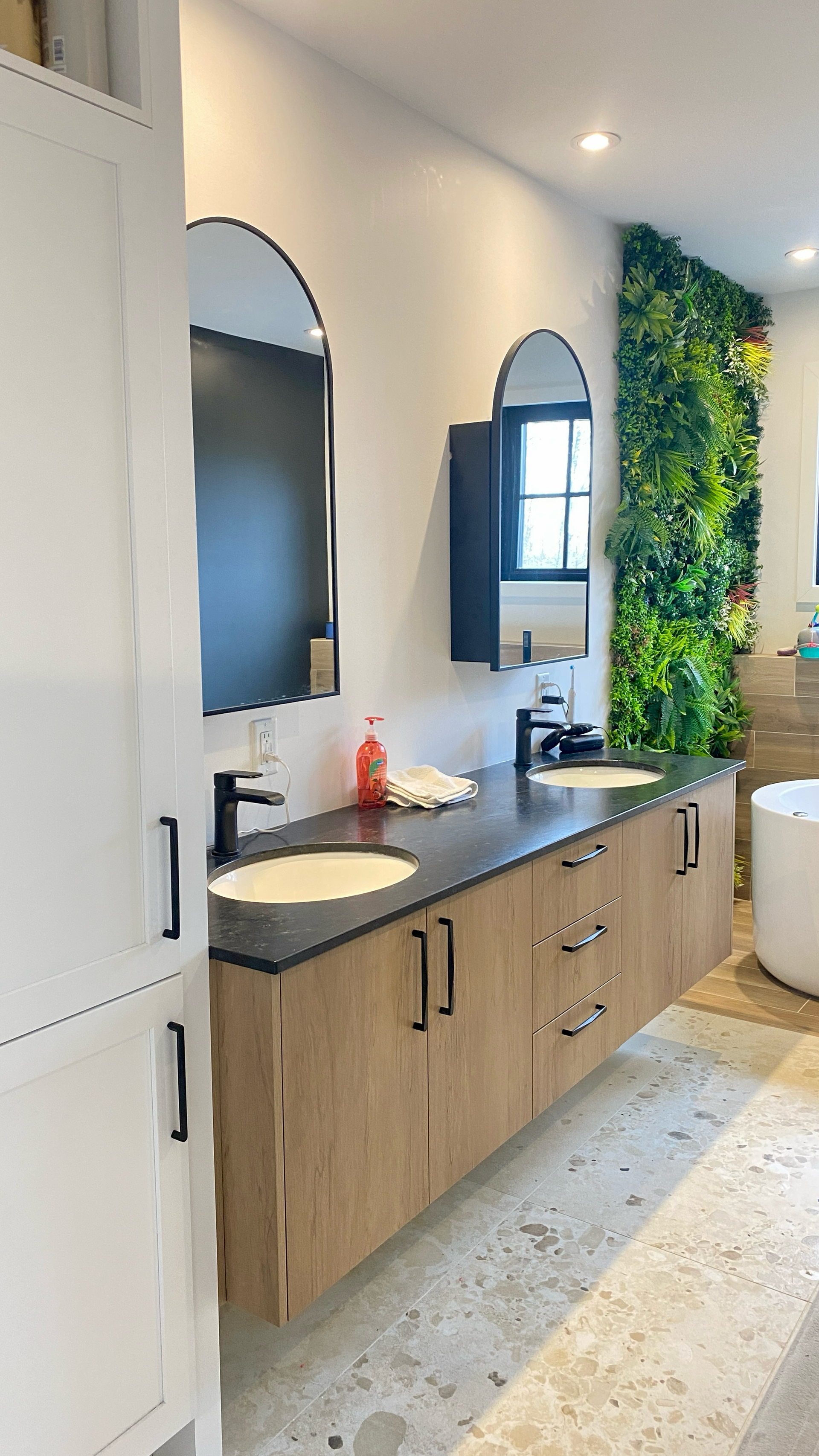 Salle de bains avec meuble-lavabo suspendu en bois, comptoir noir, miroirs arqués et mur vert.