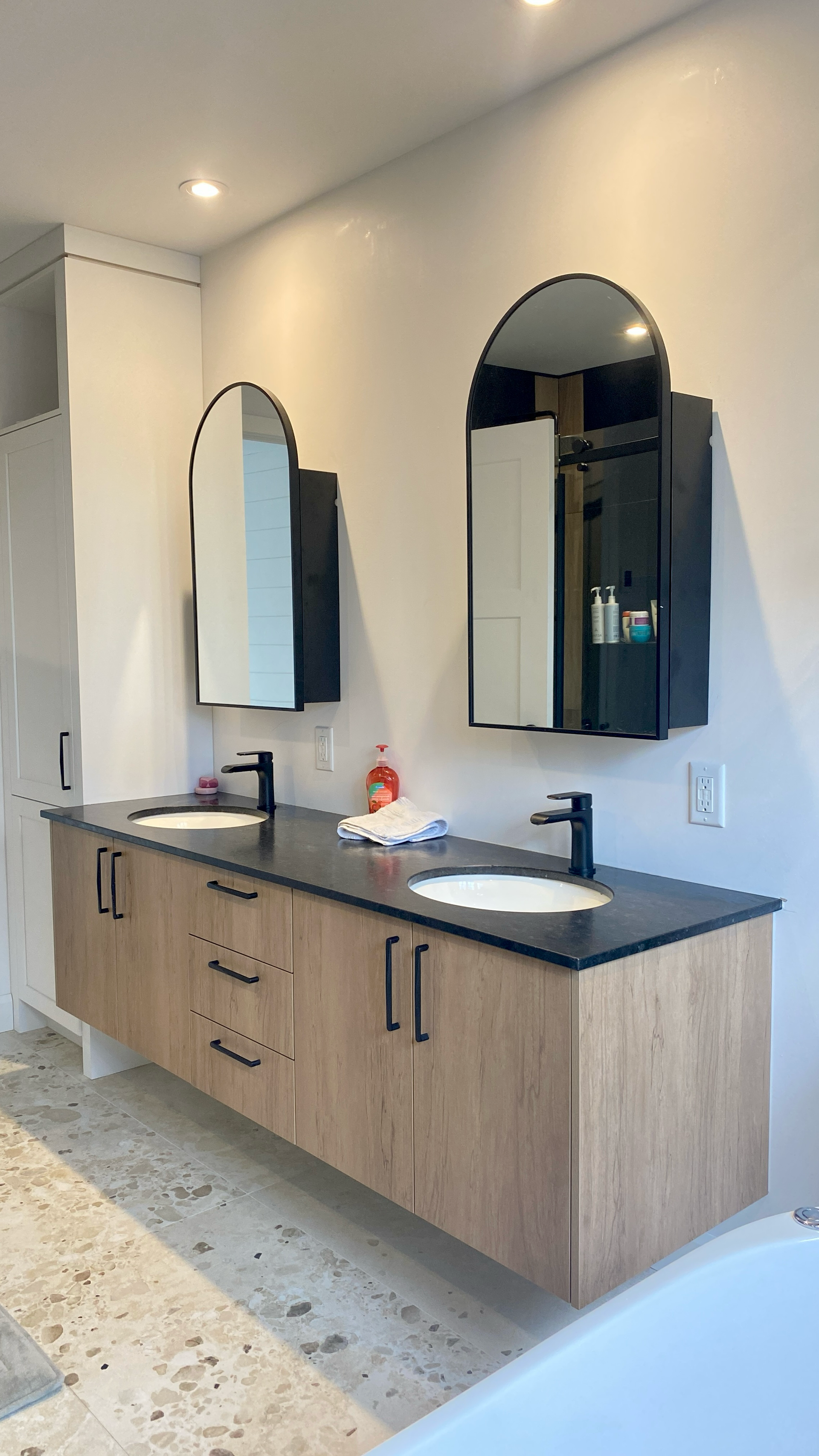 Une salle de bains moderne avec une double vasque suspendue, un comptoir noir, des miroirs arqués et des armoires en bois.