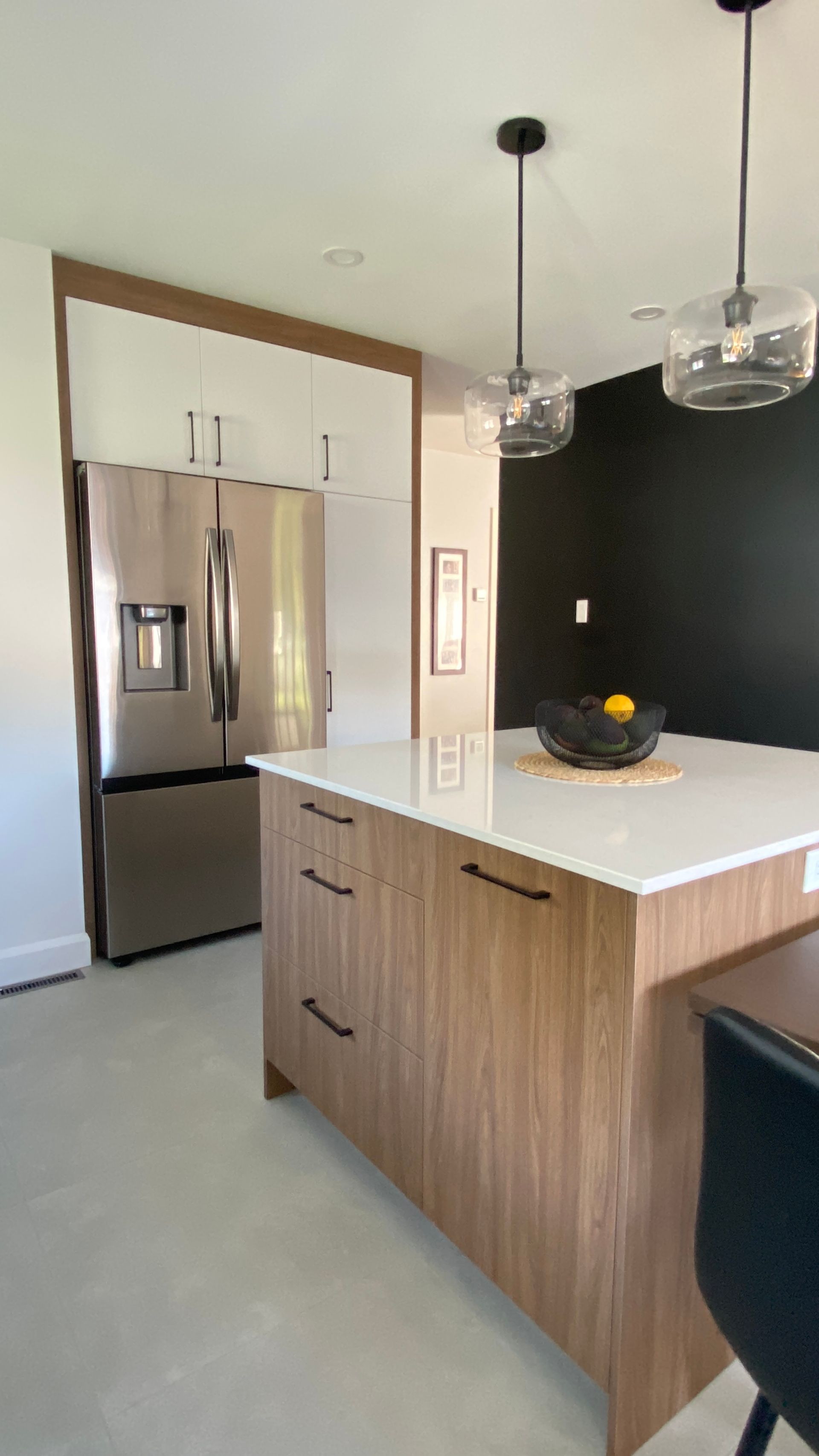 Cuisine moderne avec réfrigérateur en acier inoxydable, îlot en bois et mur d'accent noir.