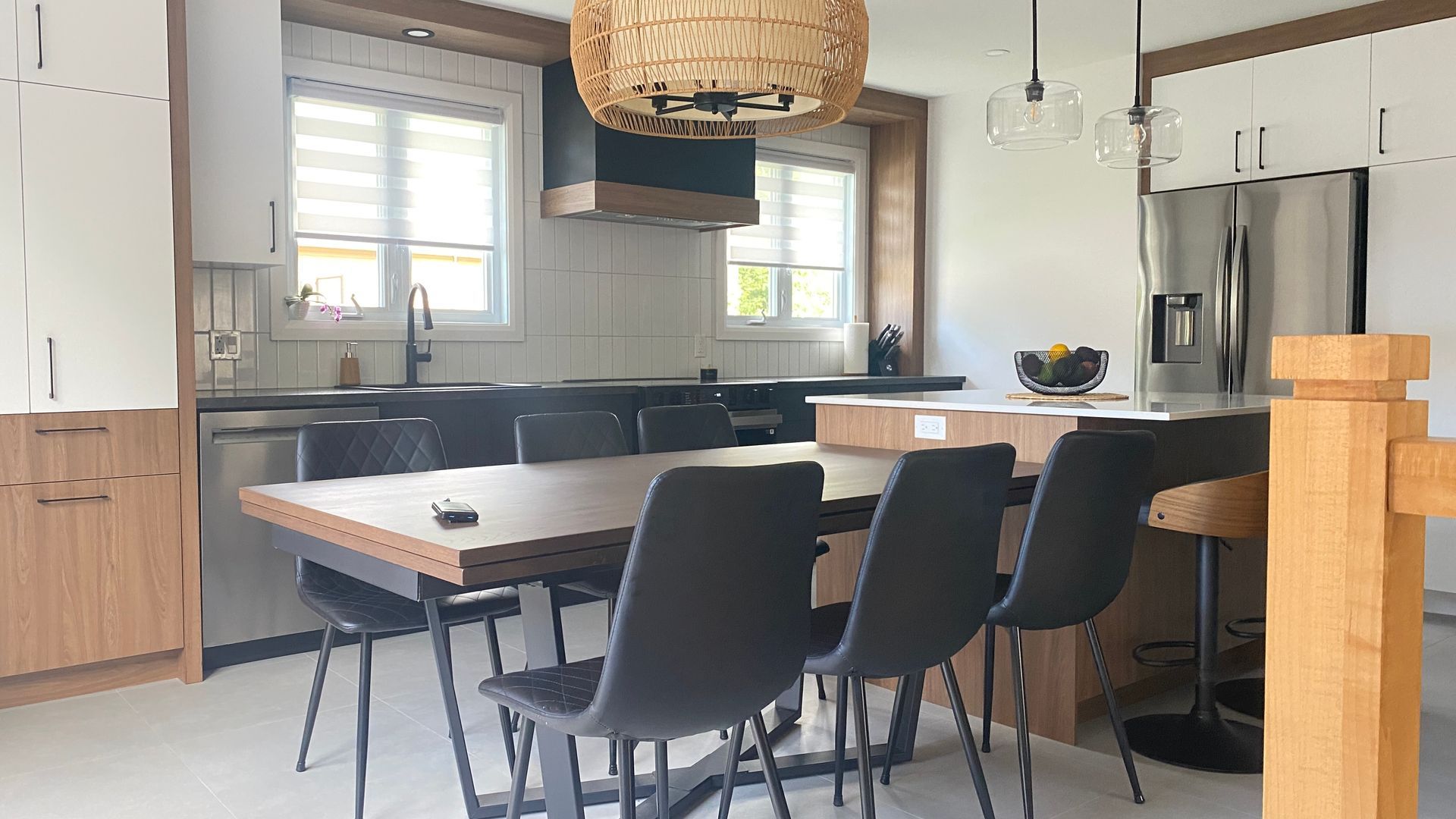 Cuisine avec table en bois et chaises noires, placards blancs et appareils électroménagers en acier inoxydable.