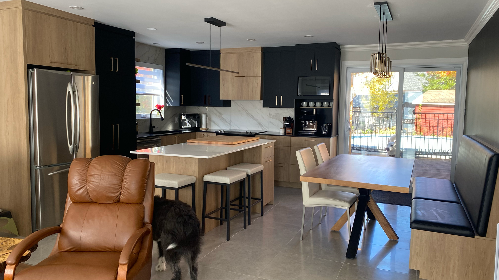 Cuisine moderne avec placards bicolores, îlot central avec tabourets, table à manger, chaise en cuir et un chien.