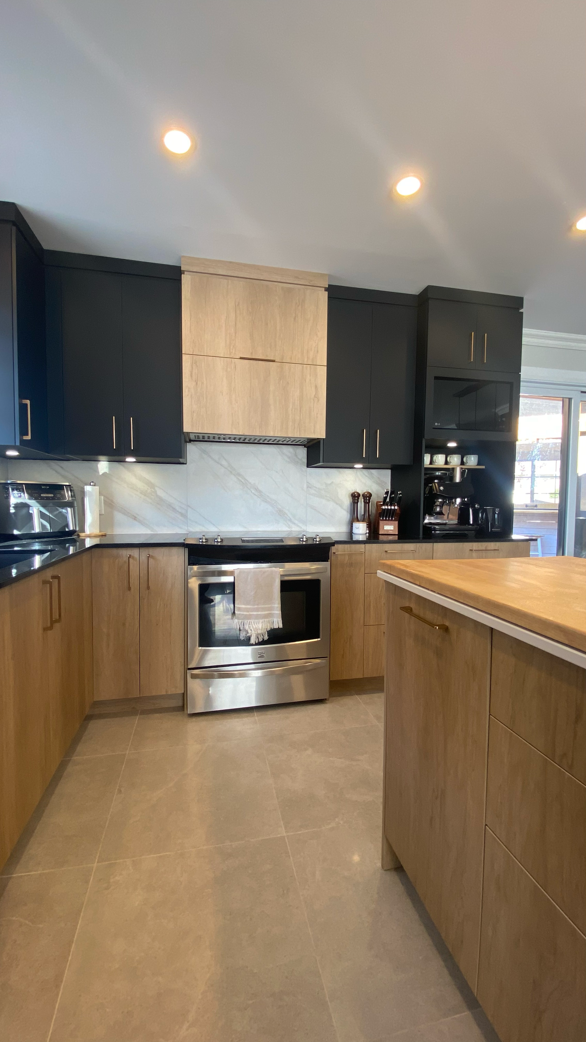 Cuisine moderne avec armoires noires et en bois, appareils électroménagers en acier inoxydable et îlot central.