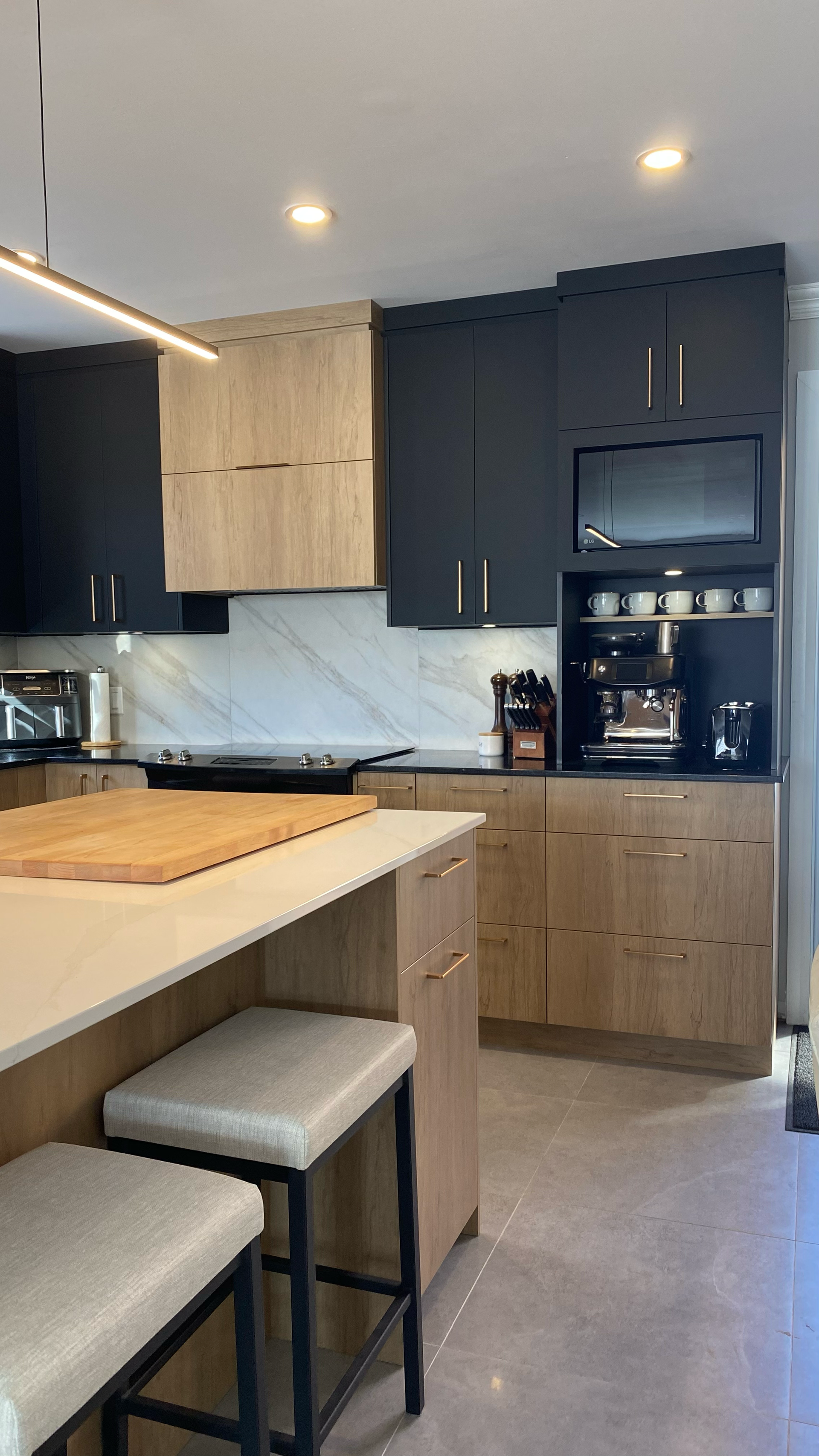 Cuisine moderne avec meubles en bois noir et clair, îlot central avec tabourets et coin café intégré.