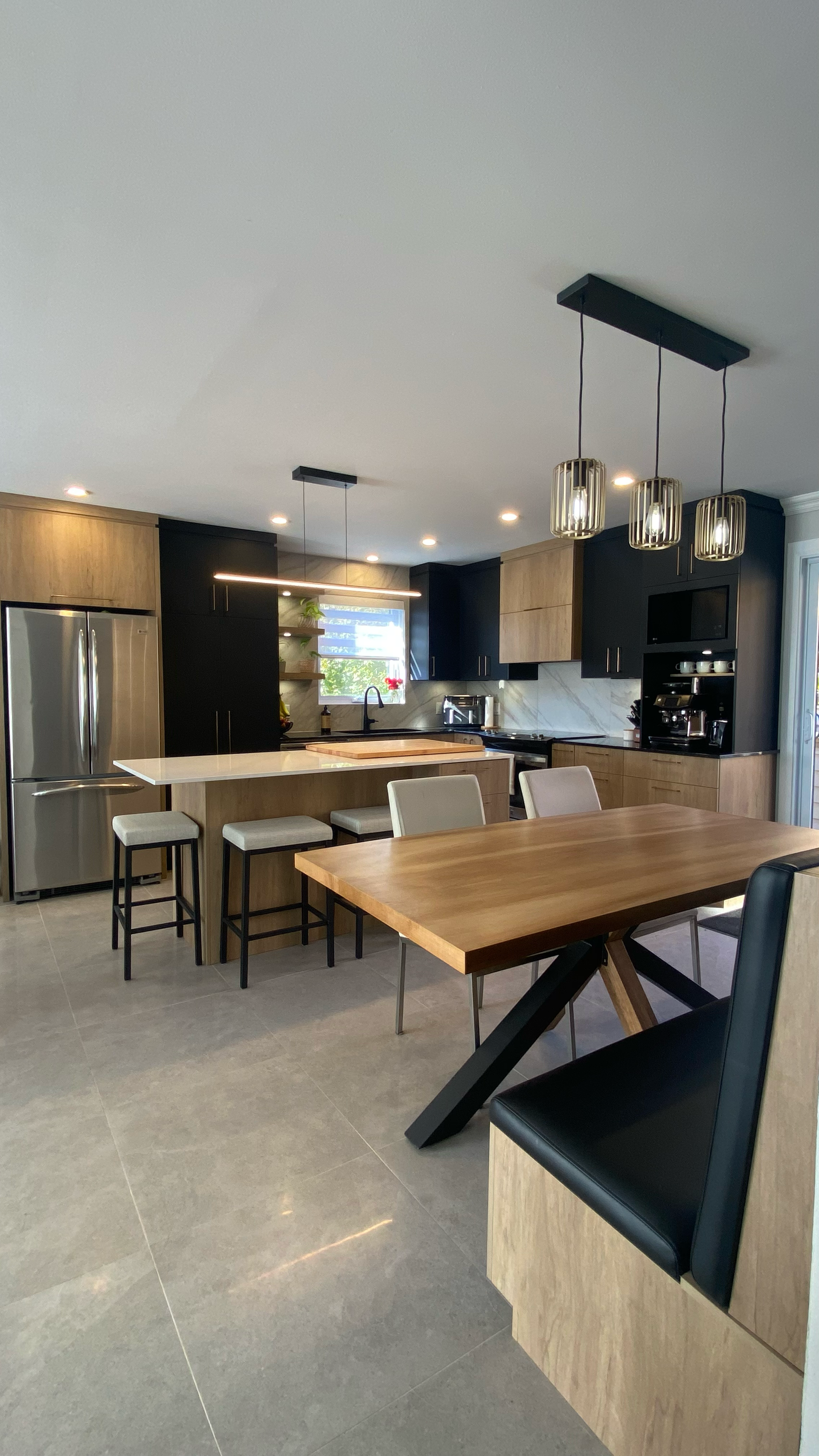 Cuisine moderne avec îlot central, armoires noires et en bois, appareils électroménagers en acier inoxydable et table à manger.