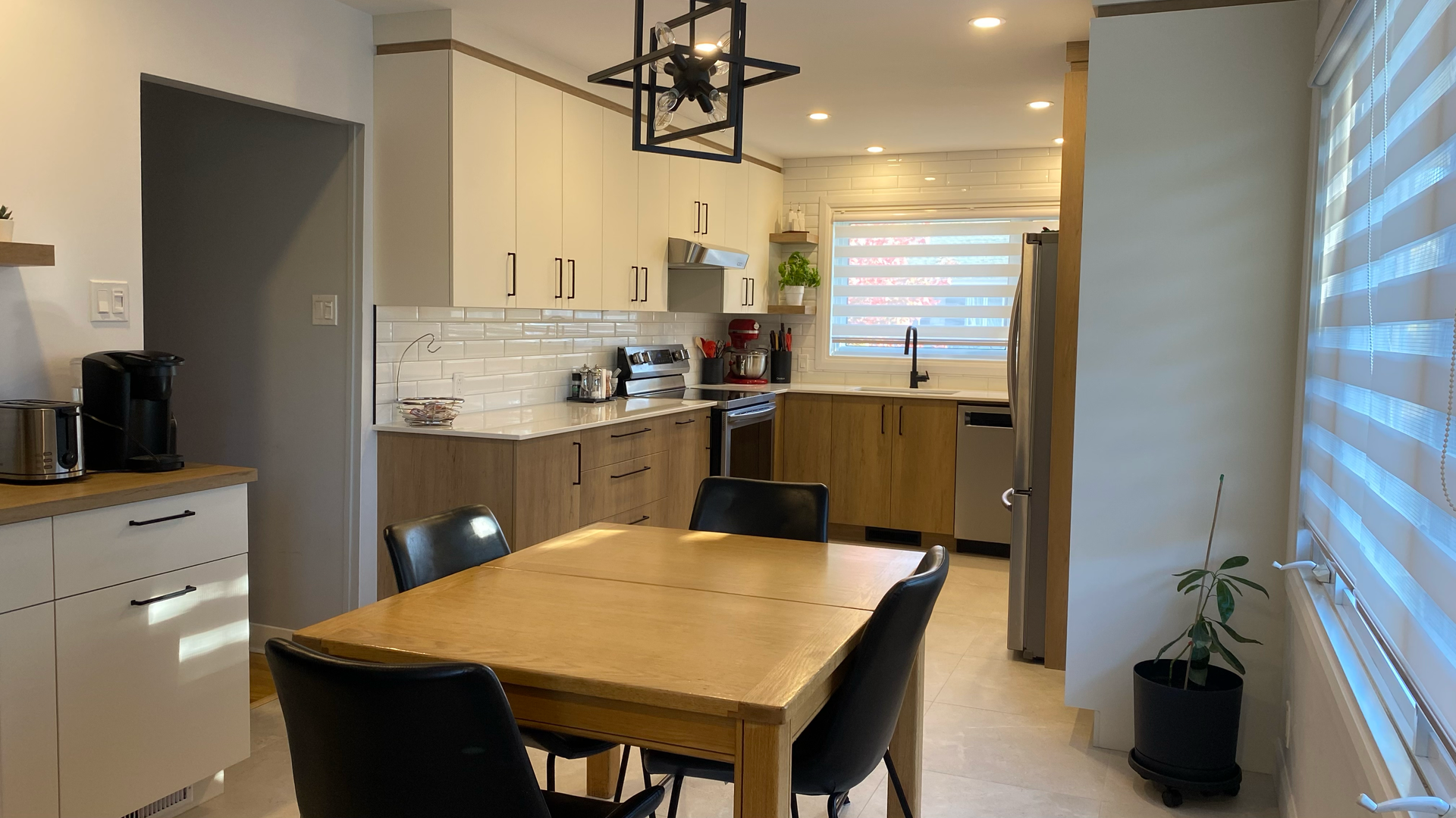 Cuisine moderne avec placards en bois clair et blancs, table en bois et chaises noires.