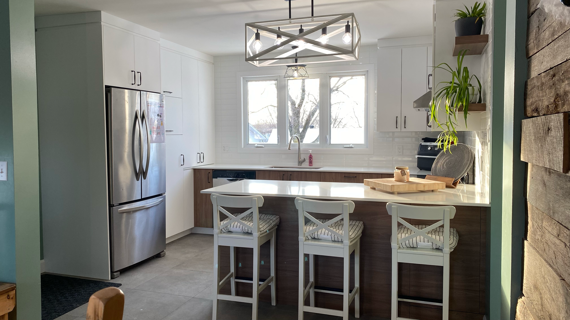 Cuisine moderne avec placards blancs, îlot central en bois foncé avec trois tabourets de bar et réfrigérateur en acier inoxydable.