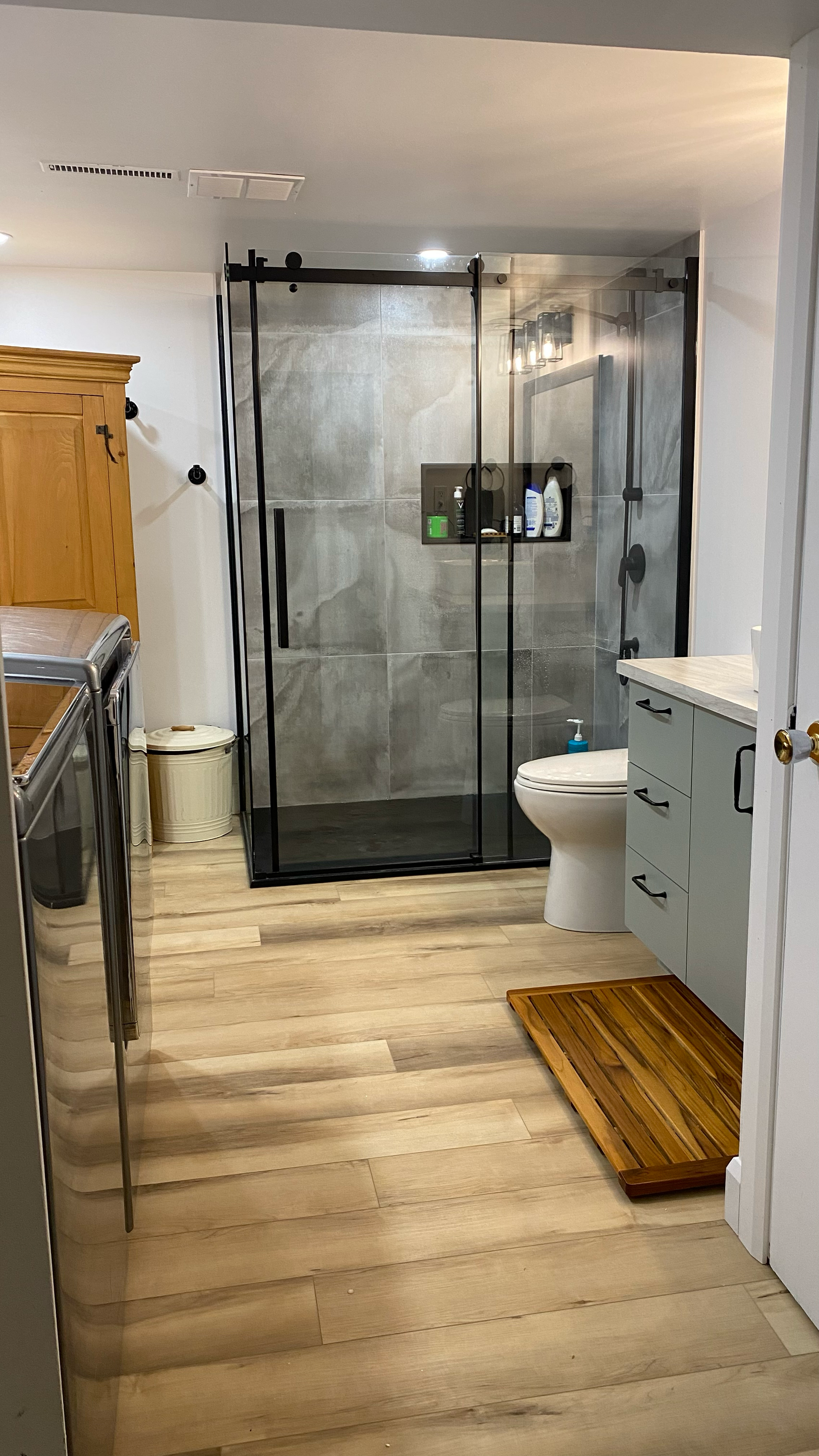 Salle de bains avec douche en verre à cadre noir, parquet clair et meuble-lavabo bleu.