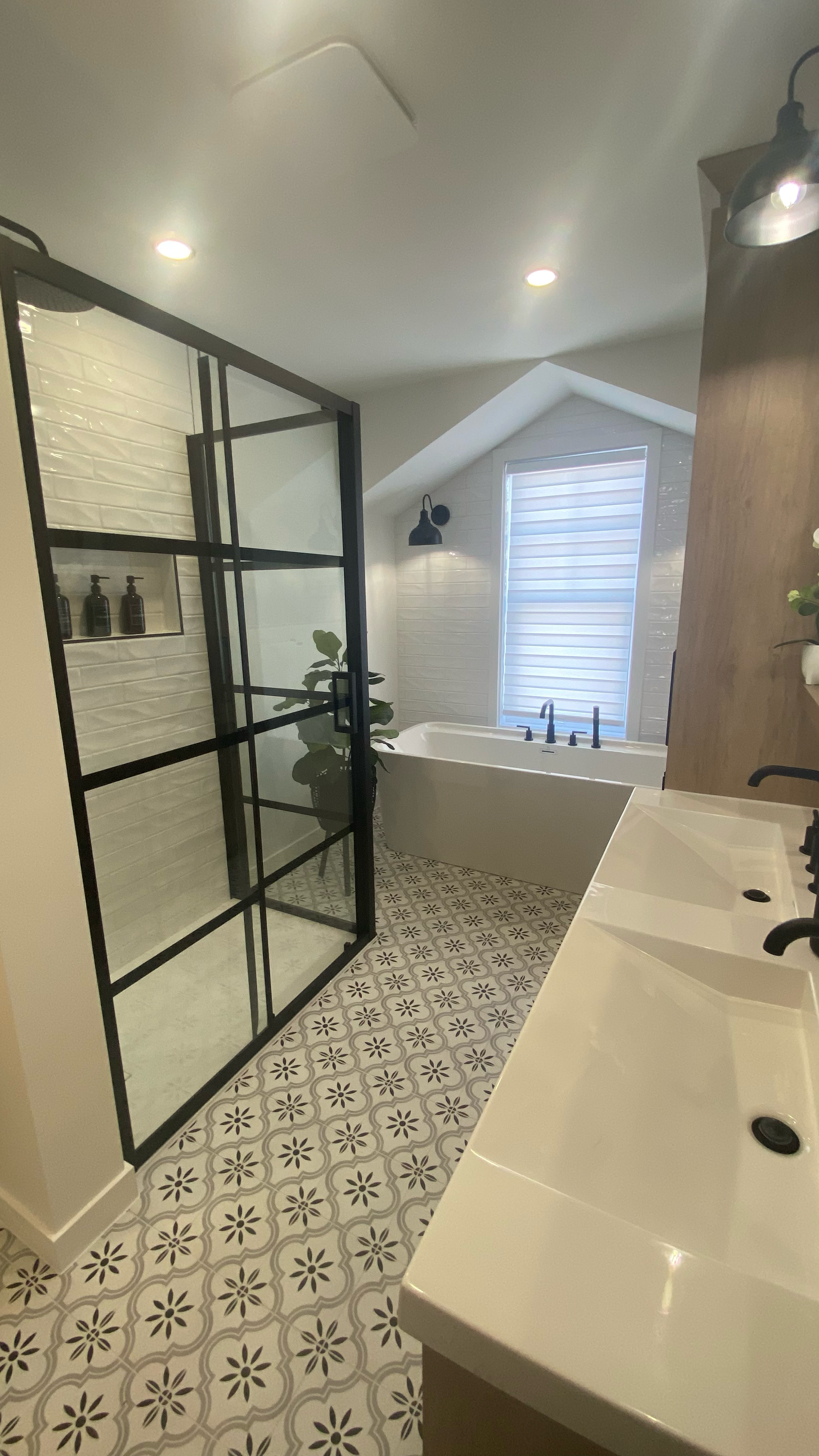 Salle de bains moderne avec douche à cadre noir, carrelage au sol à motifs, baignoire blanche et double vasque.