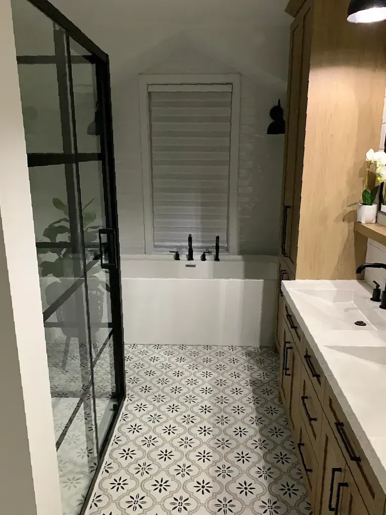 Salle de bains avec baignoire et douche, carrelage au sol à motifs, murs blancs et meubles en bois.