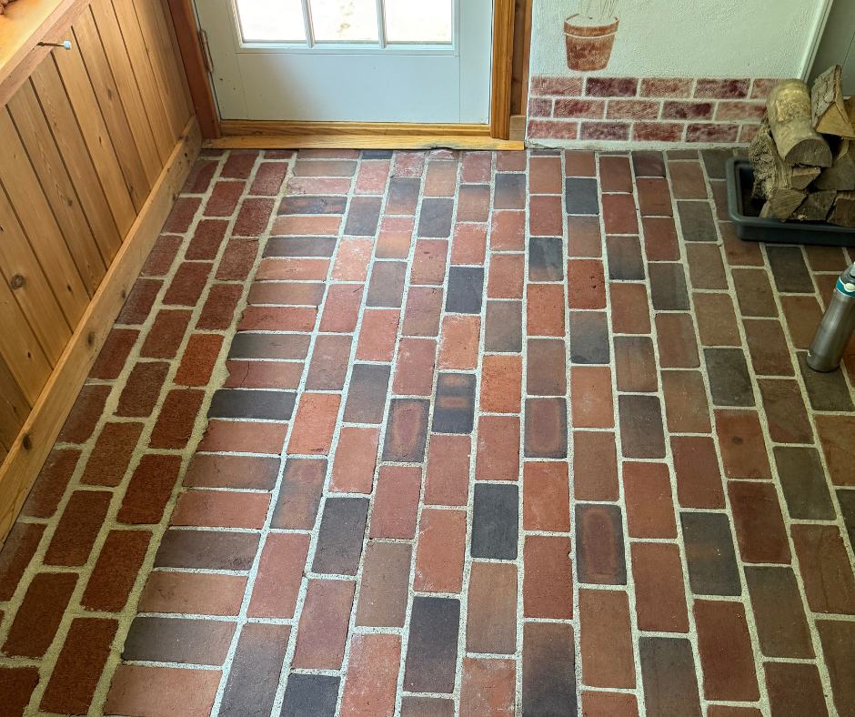 Brick-look tile floor in a small entryway with wood paneling and a glass door.