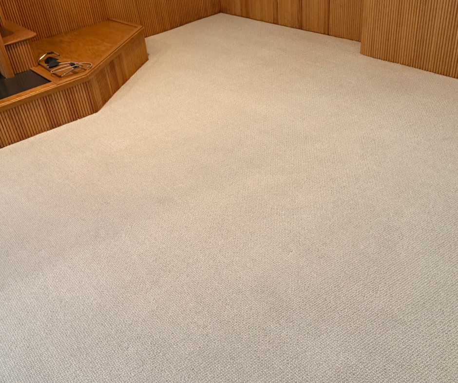 Empty beige carpeted room with wood-paneled walls and built-in corner shelving.
