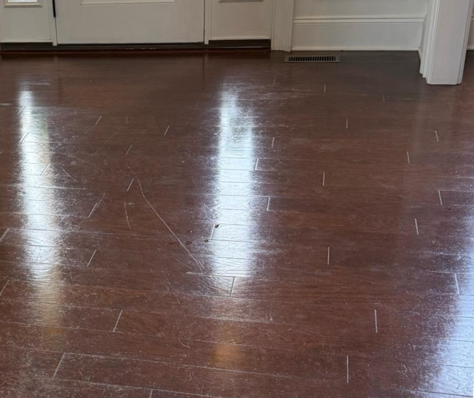 Scratched brown hardwood floor reflecting light in a room with kitchen cabinets and white trim