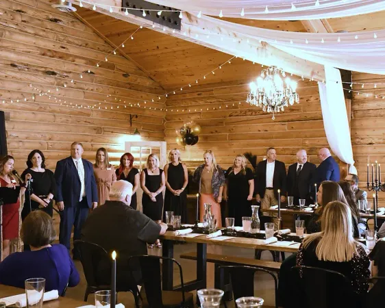 A group of people are standing in a room with tables and candles.