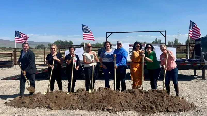 A group of people are standing in a pile of dirt holding shovels.