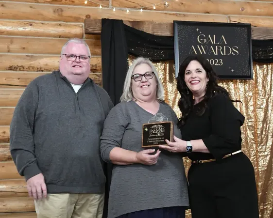 A man and two women are standing next to each other in front of a sign that says gala awards.