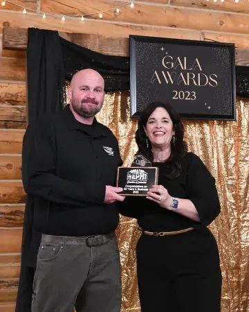 A man and a woman are standing next to each other in front of a gala awards sign.