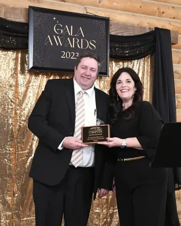 A man and woman are posing for a picture in front of a gala awards sign.