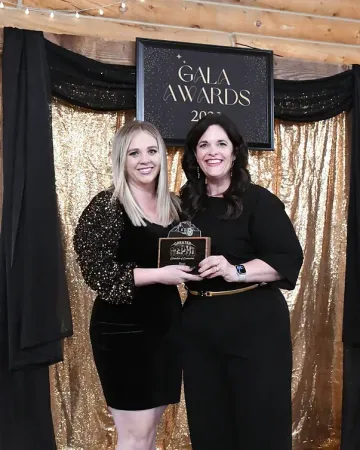 Two women are standing next to each other in front of a sign that says gala awards.