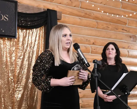 A woman in a black dress is holding a trophy in front of a microphone.