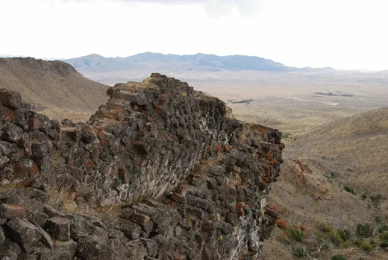 A large rock formation in the middle of a desert with mountains in the background.
