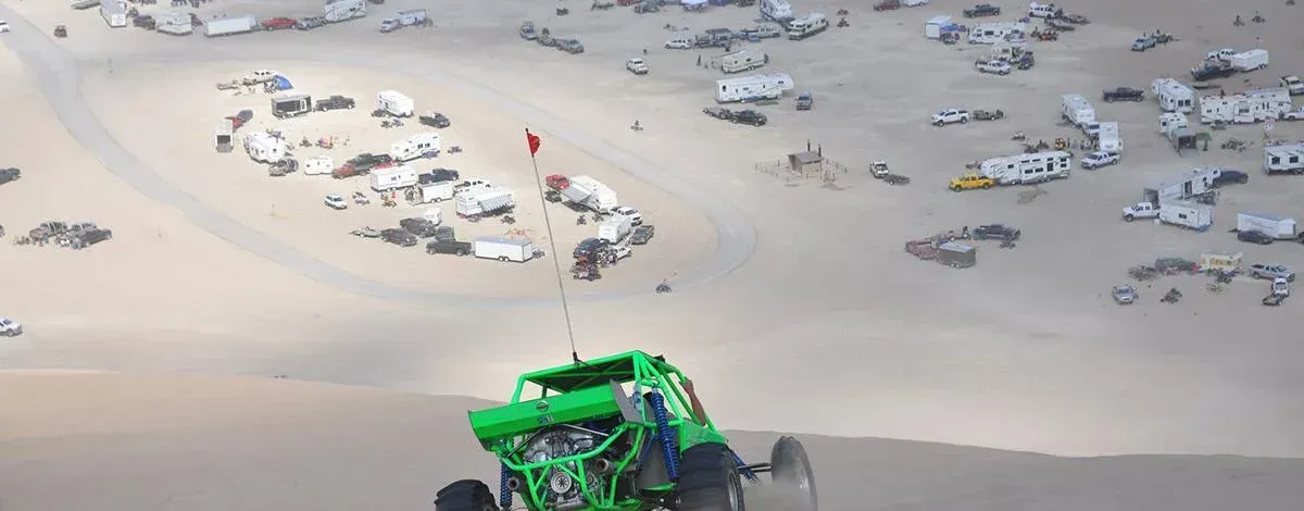 A green buggy is driving down a dirt road in the desert.