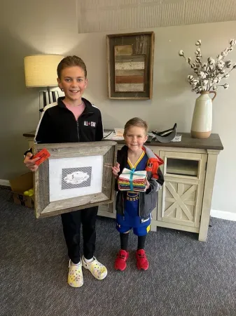 Two young boys are standing next to each other in a living room holding gifts.