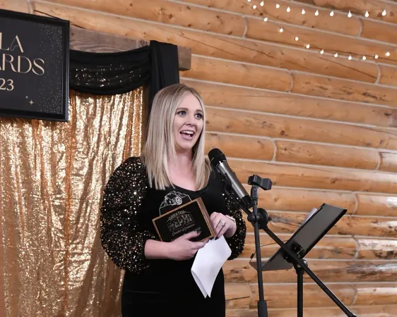 A woman is standing in front of a microphone holding an award