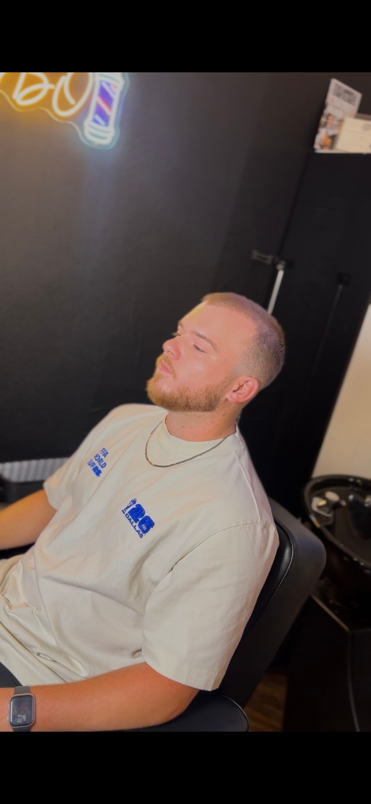 Man in a white shirt reclining in a chair against a dark wall with neon lights overhead