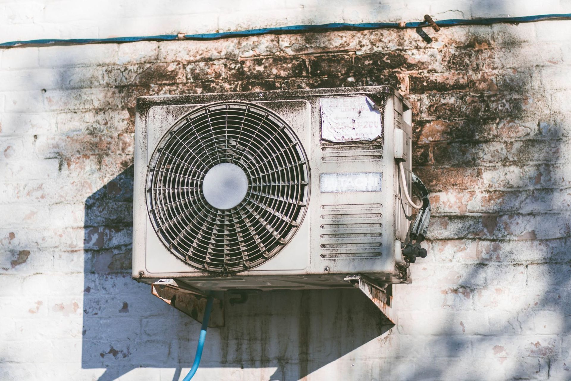 An air conditioner is hanging on a brick wall.