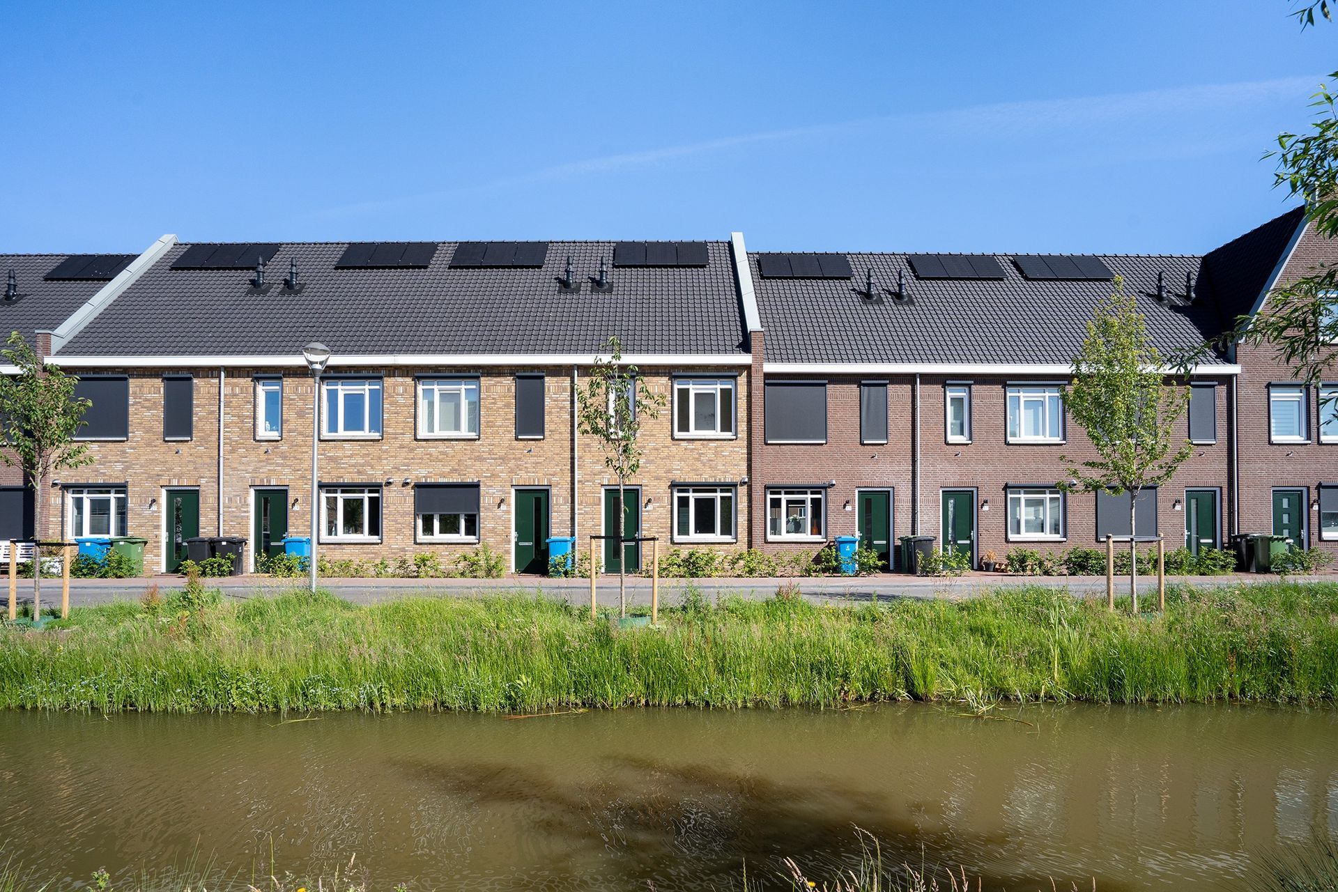 Rij rijtjeshuizen met zonnepanelen op de daken, gelegen naast een kanaal.
