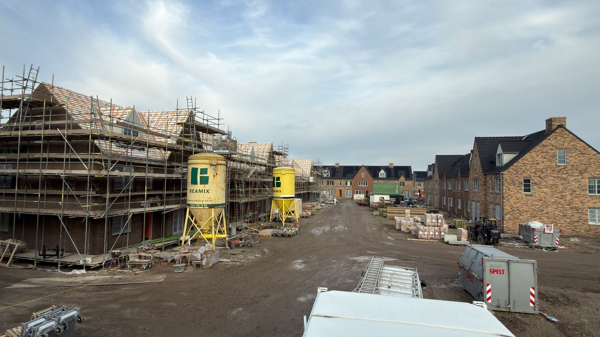 Bouwplaats met steigers en bouwmaterialen; woongebouwen in aanbouw.