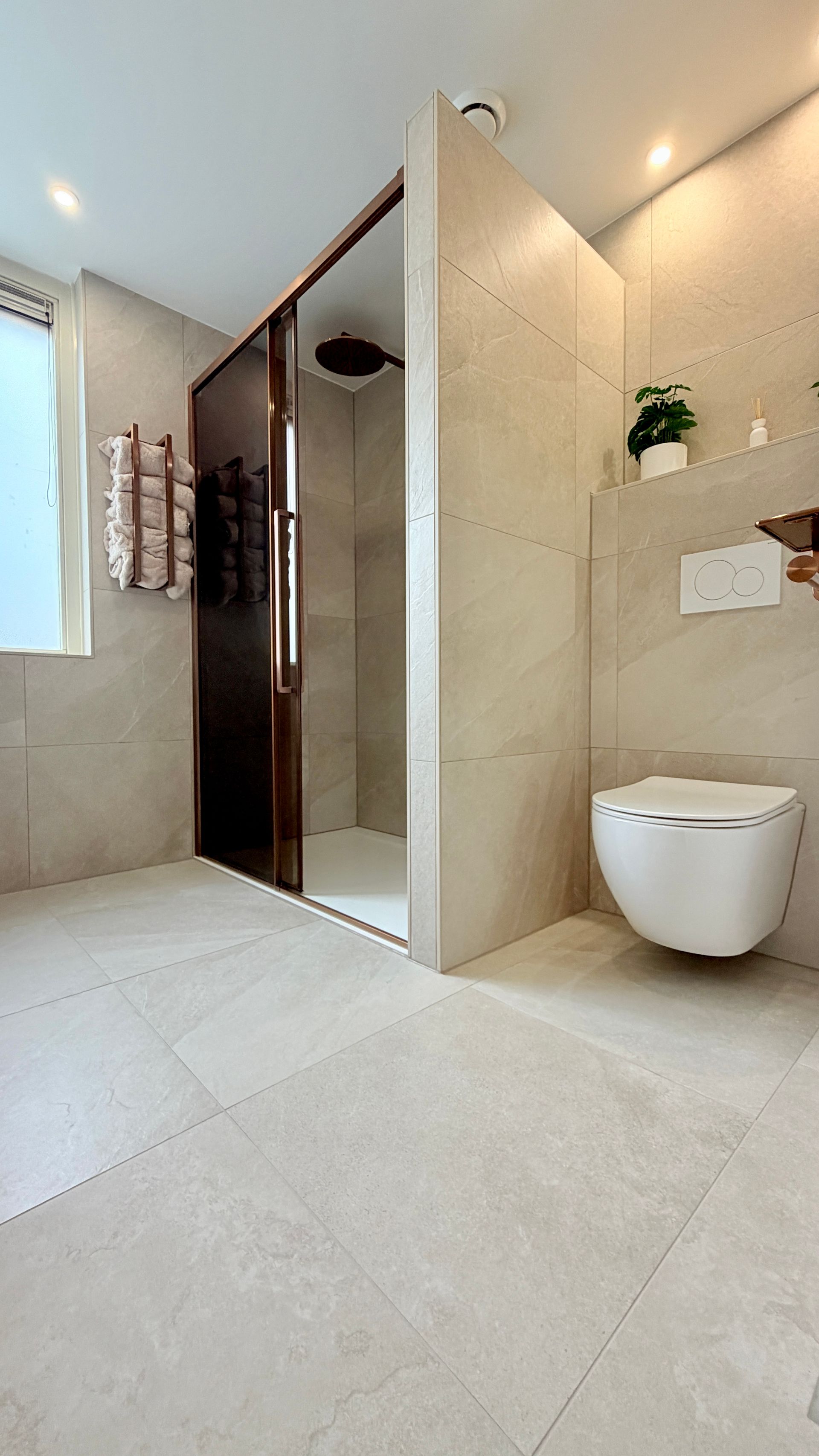 Moderne badkamer met beige tegels, glazen douchecabine en wandtoilet.