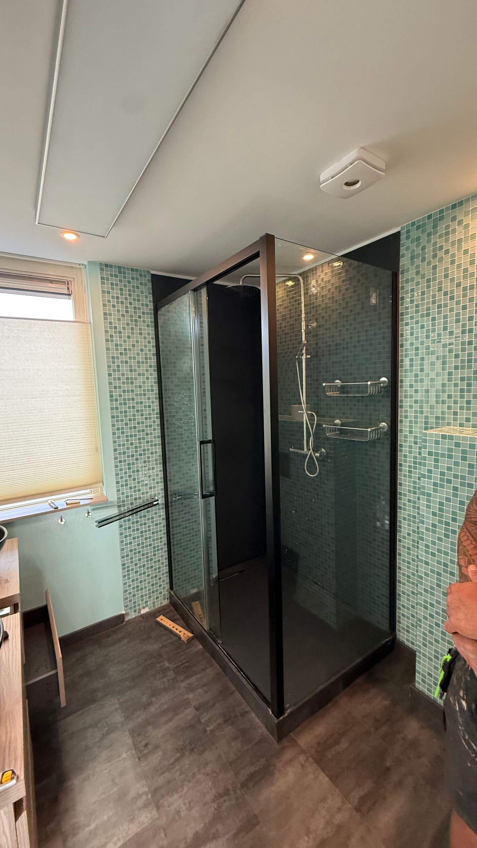 Moderne badkamer met glazen douchecabine, betegelde muren en een decoratief rolgordijn.