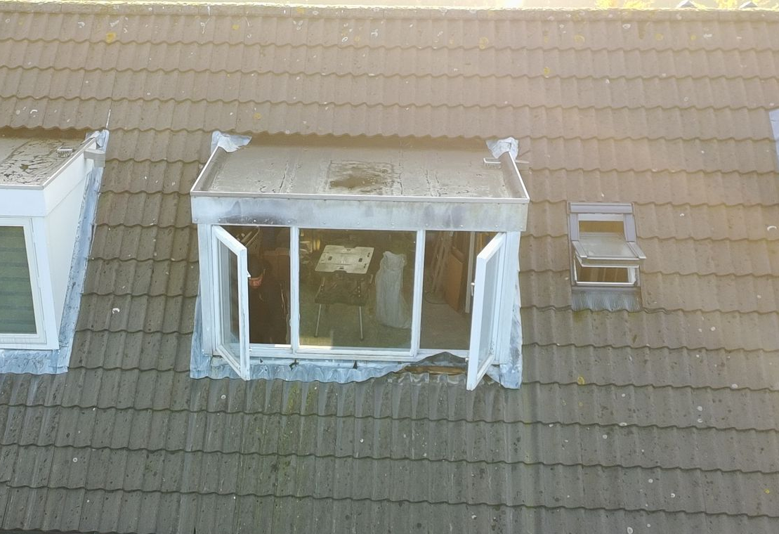 Dak met een open raam en een klein dakraam. Verweerde dakpannen en metalen dakrandafwerking.