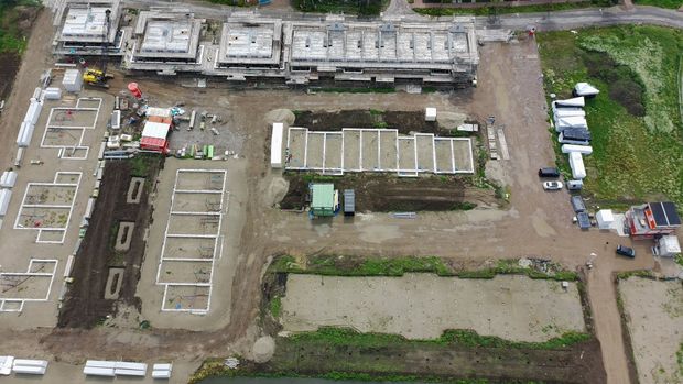 Bouwterrein: diverse gebouwen in verschillende stadia van voltooiing. Fundamenten, bekisting en bouwmachines zijn zichtbaar.