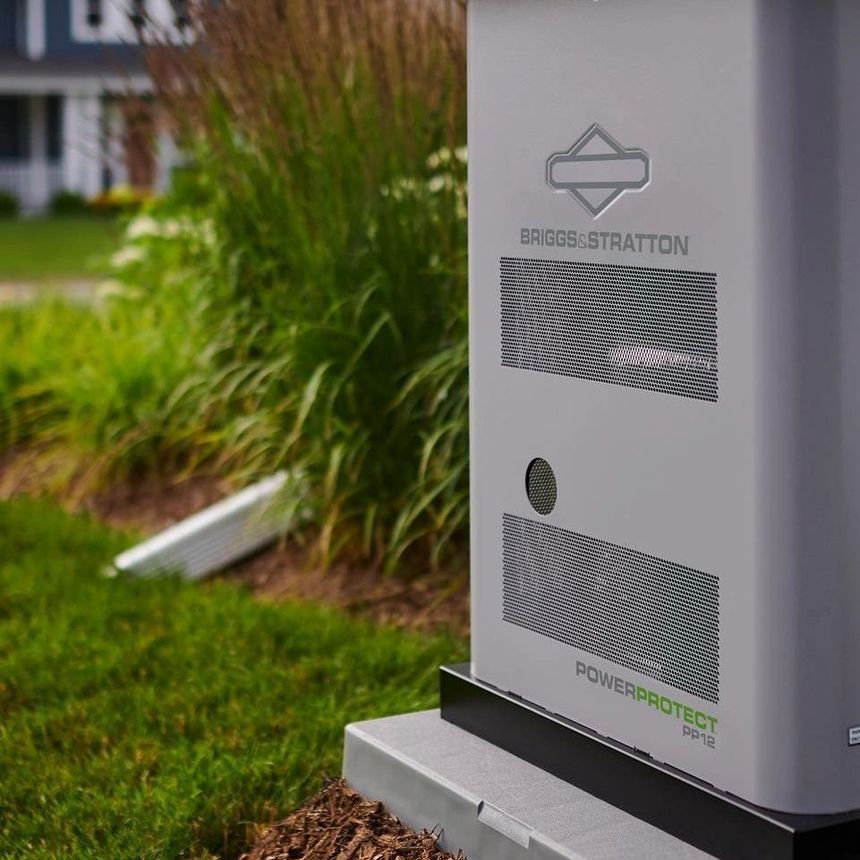 Outdoor gray utility cabinet with vented panels beside green landscaping and a house.