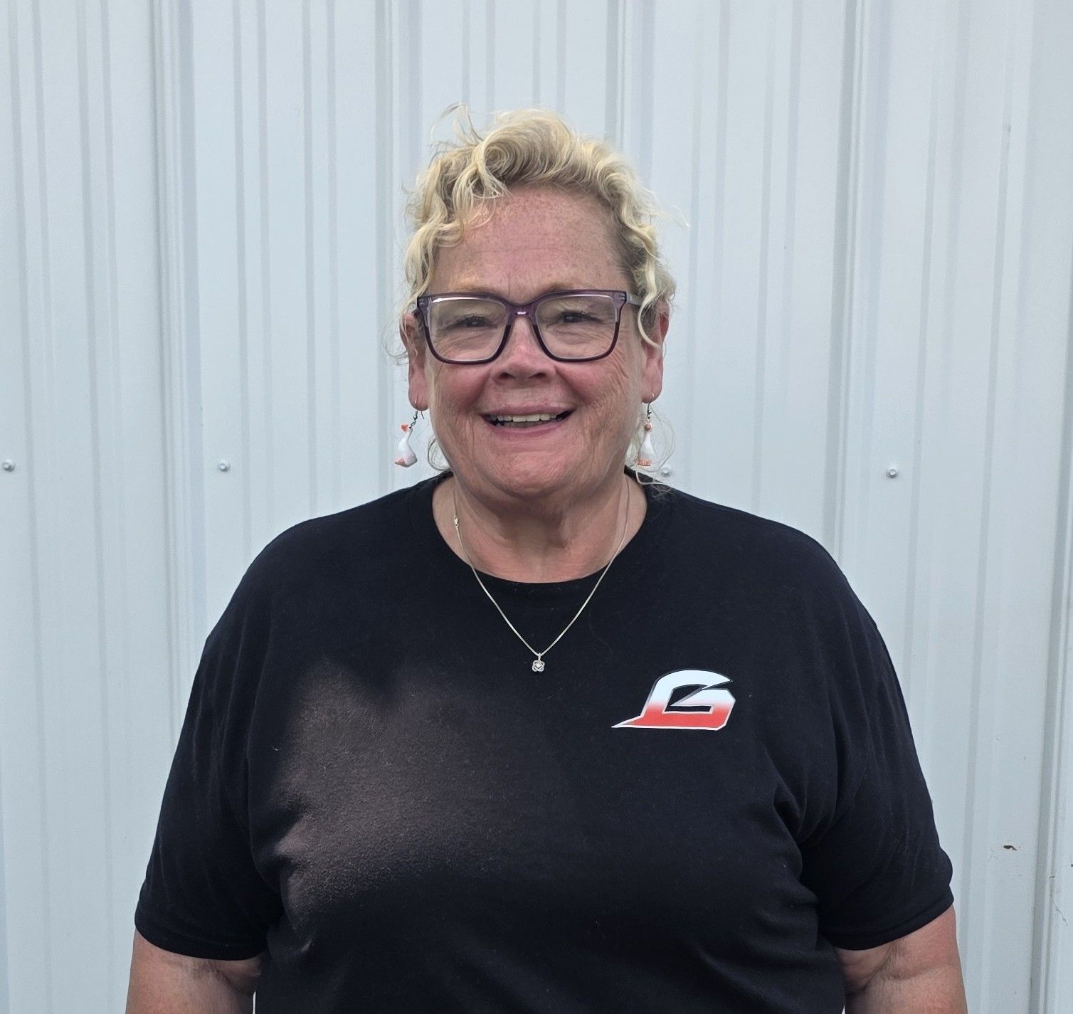 Smiling person in black shirt and glasses standing before a white corrugated wall