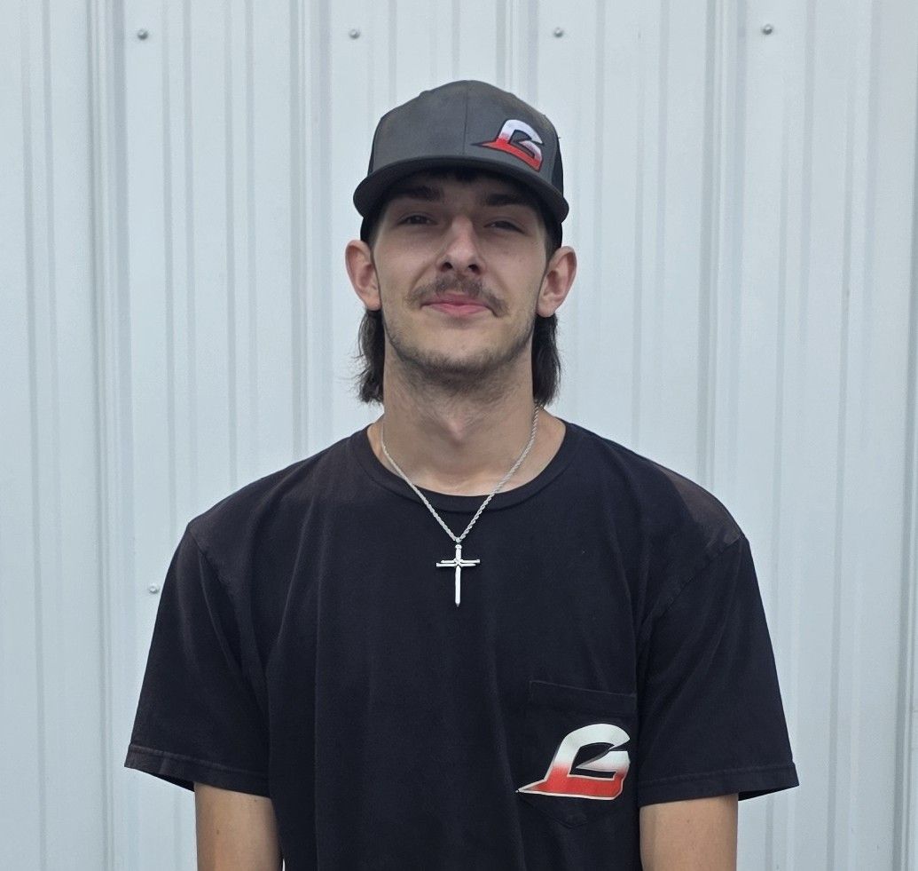 Young man in a black cap and T-shirt standing against a light corrugated metal wall.
