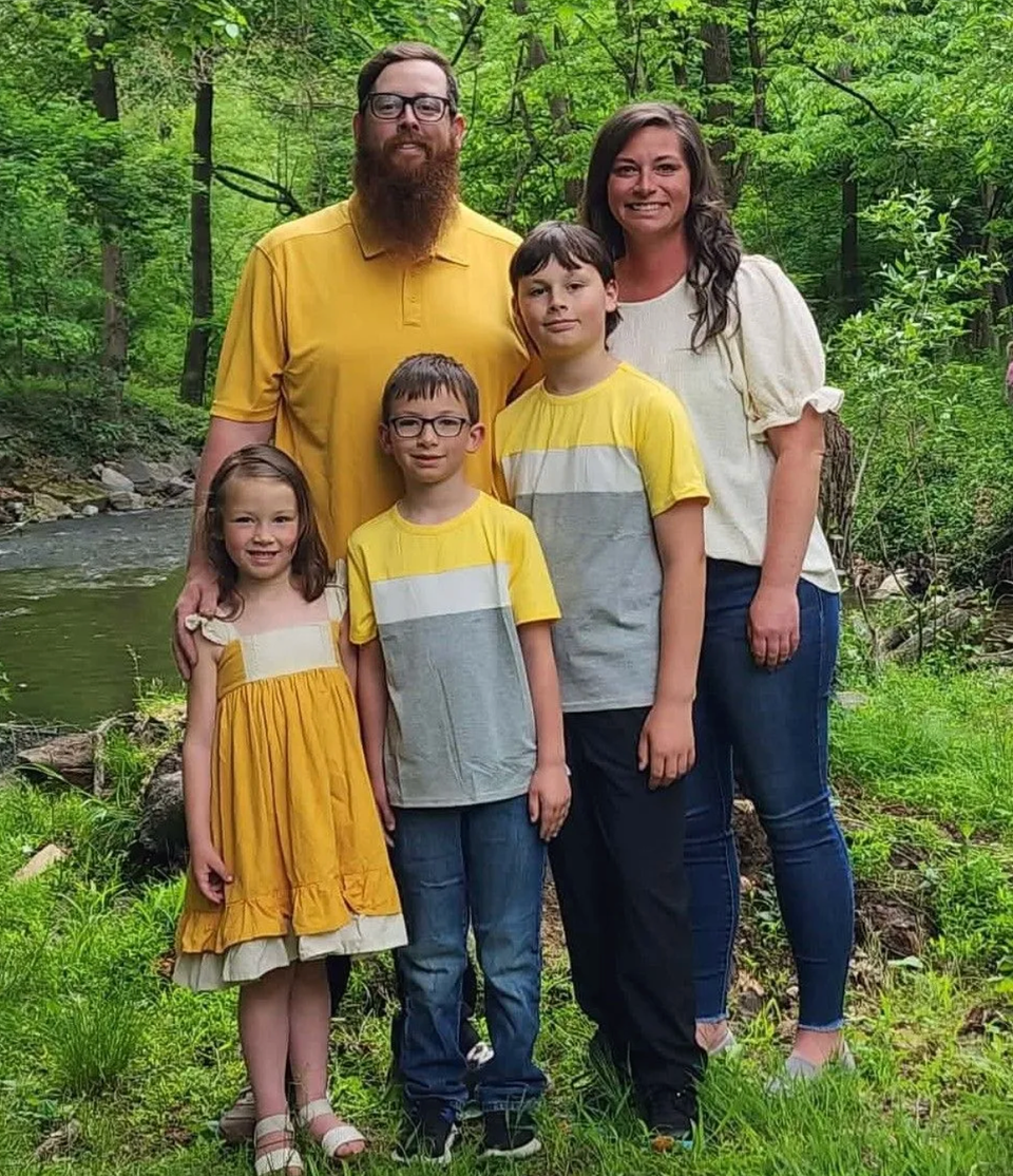Family of four and two children posing outdoors in a green wooded area, smiling at the camera.