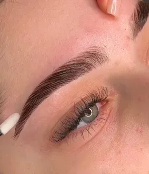 Close-up of an eyebrow being shaped with a white tool above a green eye