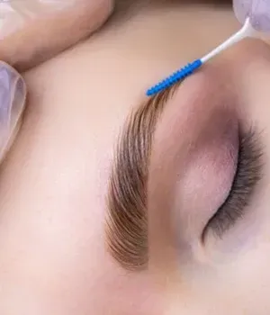 Close-up of an eyebrow being brushed with a blue spoolie on a closed eye.