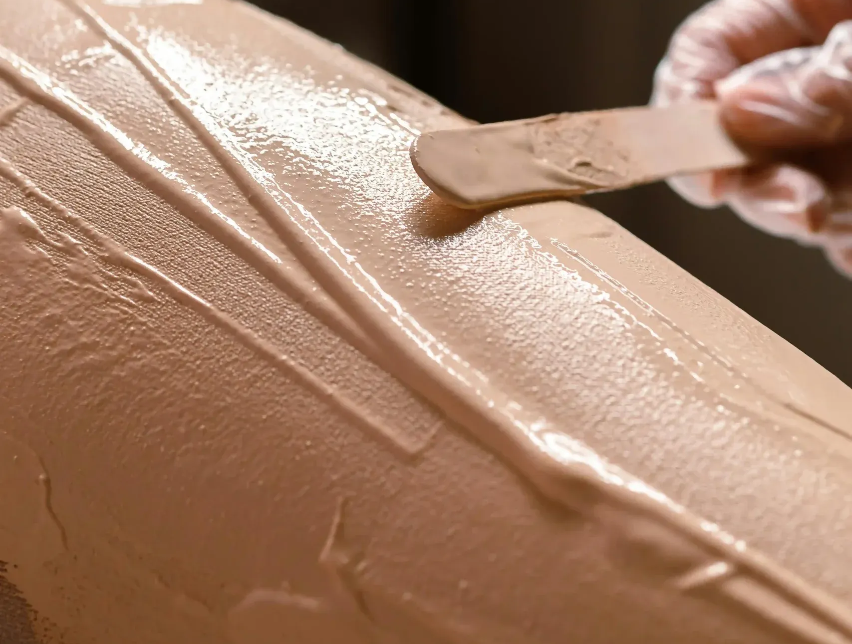 Close-up of a hand spreading smooth tan frosting on a cake with a spatula